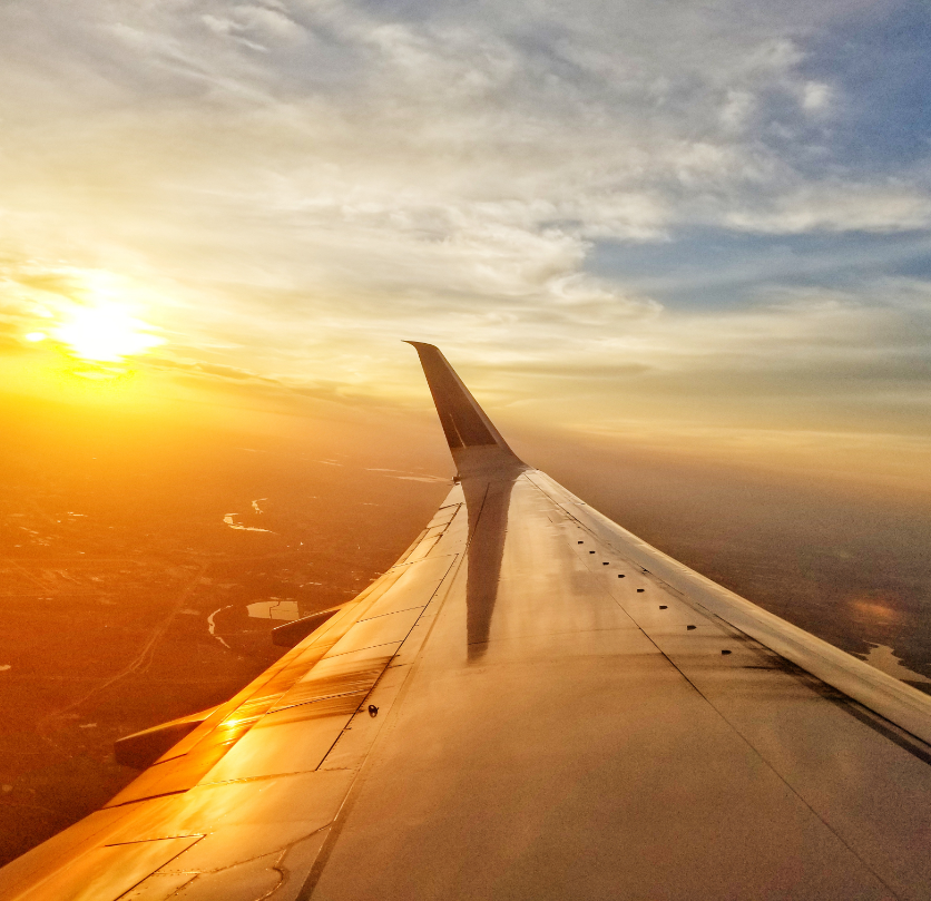 A golden sunrise illuminates the wing of an airplane as it soars above winding rivers and rolling landscapes below. This captivating view captures the excitement of travel, showcasing the endless possibilities provided through vacation fundraising to support meaningful causes.