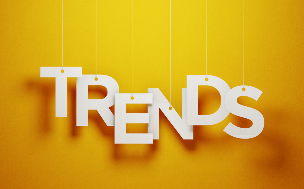 Bold white letters spelling "TRENDS" are suspended by strings against a vibrant yellow background, creating a visually striking composition. This dynamic design symbolizes emerging ideas and innovations, such as the growing popularity of vacation fundraising to create impactful and memorable experiences.