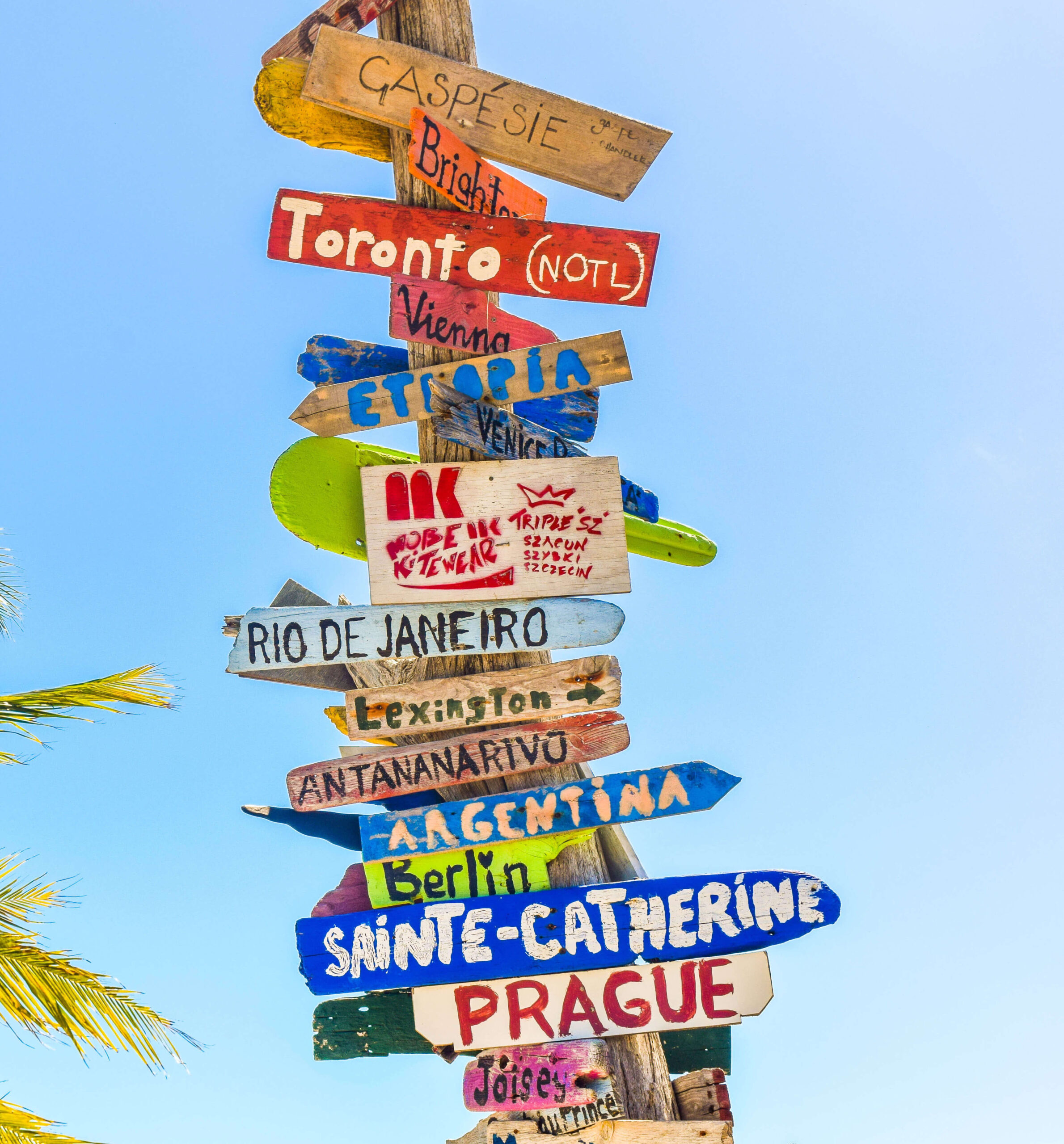 Colorful wooden signpost with arrows pointing to various vacation package locations, including Toronto, Vienna, and Rio de Janeiro, against a clear blue sky.